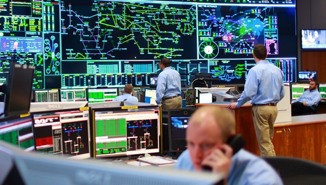 Industrial control room with operators monitoring large digital displays showing real-time electrical and process system data.